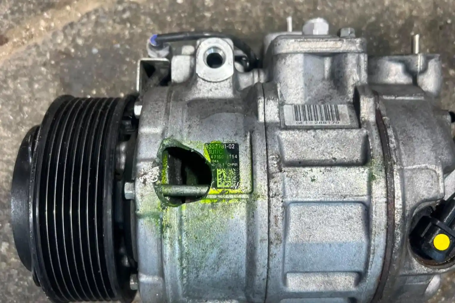 A cracked vehicle AC compressor with green UV leak detection dye, highlighting the need for car AC repair.