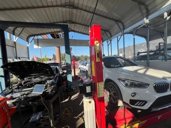 A white BMW SUV on a lift beside a car connected to computer diagnostics for professional auto repairs in Brandon, FL by BMW and More Auto Care.