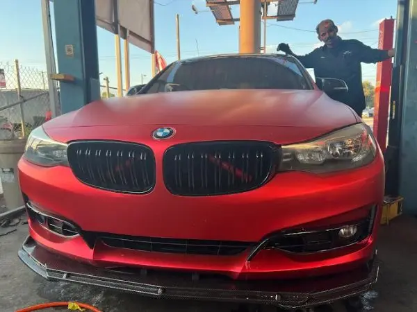 A mechanic posing beside a custom matte red BMW sedan ready for professional auto repairs in Carrollwood, FL by BMW and More Auto Care.