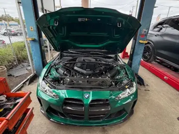 Green BMW M3 on a service lift with open hood undergoing professional auto repairs in Clearwater, FL by BMW and More Auto Care.